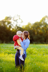Fototapeta premium Young mother kissing her little son during walk in the flowers field