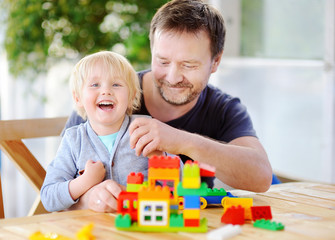 Little boy with his father playing with colorful plastic blocks at home