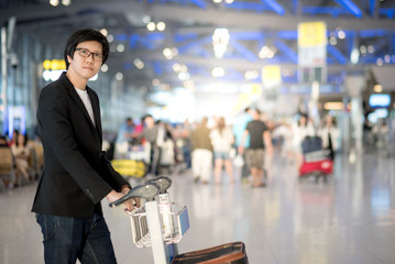 Young asian man with his luggage on airport trolley waiting for check in at airline counter in the international airport terminal, business travel concept