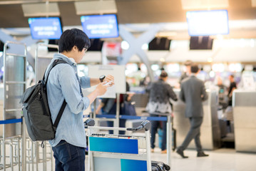 young asian man waiting for check in and dropping his luggage at airline check-in counter of international airport terminal