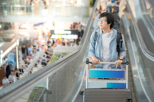 Young Asian man with airport trolley on escalator, walking to check-in counter in the international airport terminal. travel abroad on vacation