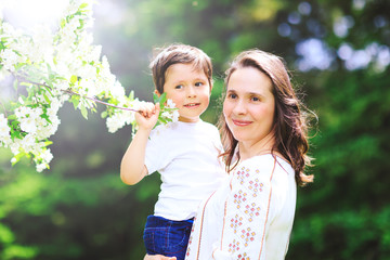 Beautiful mother with lovely son on background of spring blossom park. Happy mom and cute son celebrate mother day or women day. Spring blossom tree and attractive woman with lovely kid.