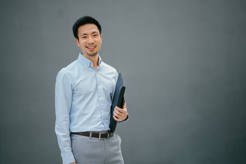 Portrait of happy smiling young businessman, standing on  a plain gray background while holding his...