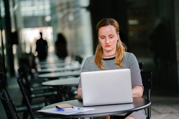 Portrait of a young but confident and mature Russian woman working on her laptop and some documents while sitting at a table in her office. She's too focused and serious as she types on her computer.