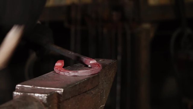 Master is forming an iron shoe for horse in a studio of forgery. He is putting it on an anvil and beating, close-up of hands