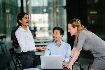 Portrait of a team meeting between a diverse group of business people, lawyers, consultants or other professionals. They are looking at a laptop and smiling as they discuss a topic in a group. 