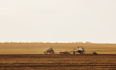 Obraz premium a tractor with a trailer plowing field for sowing of agricultural machinery is preparing for a new crop.