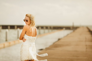 Fototapeta na wymiar woman in white short wedding dress. bride in glasses with blond hair standing at the pier.