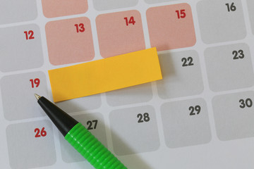 Green pen points to a nineteen number of calendar and have blank yellow note paper.