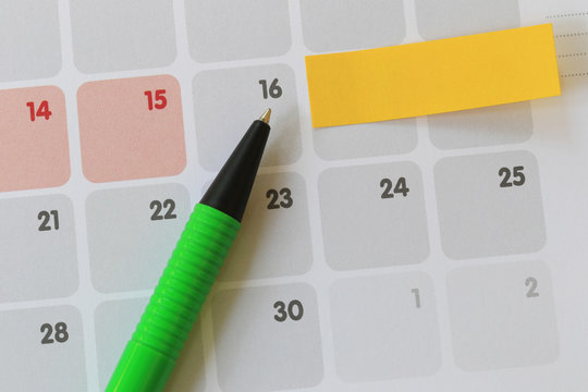 Green pen points to a sixteen number of calendar and have blank yellow note paper.