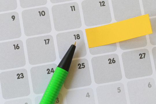 Green pen points to a eighteen number of calendar and have blank yellow note paper.