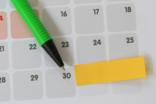 Green pen points to a thirty number of calendar and have blank yellow note paper.