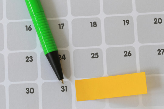 Green pen points to a thirty one number of calendar and have blank yellow note paper.