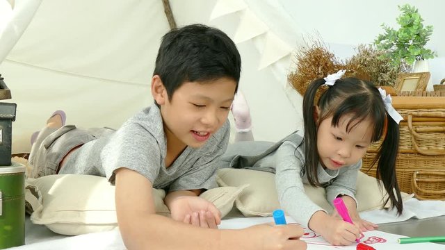 Young asian girl and boy drawing picture by crayon and pencils on the floor at home
