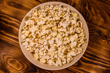 Obraz na płótnie Canvas Ceramic plate with popcorn on wooden table. Top view