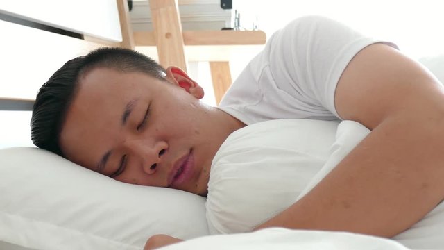 Young asian man yawning and stretching sitting in bed at home in the morning 