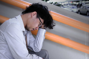 Side view of stressed depressed young Asian business man suffering from severe depression.
