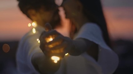 Loving couple wrapped in fairy lights caressing and kissing on romantic rooftop date at sunset