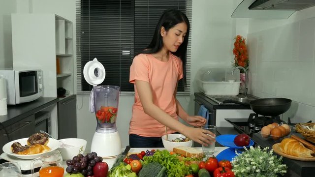 4k of young woman making smoothies with blender in kitchen