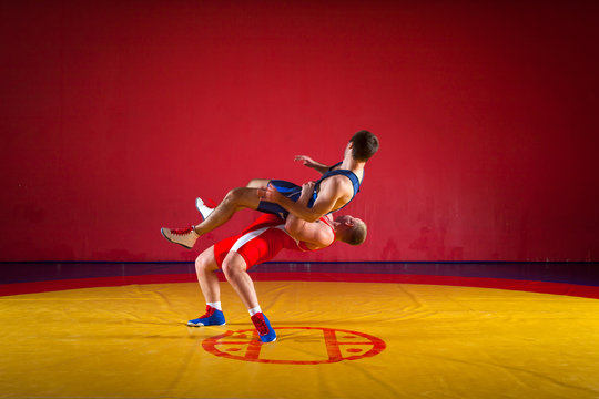 Two strong wrestlers in blue and red wrestling tights are wrestlng and making a  hip throw wrestling on a yellow wrestling carpet in the gym. Young man doing grapple.