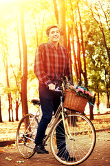 Man on bicycle with flowers basket is riding summer park outdoor in sunlight. Beginning of new season of romance. Sunlight in sunset or sunrise.