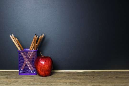 Pencil in basket and red apple on wood table with Blackboard (Chalk Board) as background with copy space. Education and Back to school concept.
