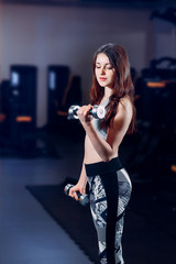 a beautiful sportswoman is engaged in dumbbells in the gym
