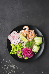 Fresh seafood recipe. Shrimp poke bowl with fresh prawn, brown rice, cucumber, pickled sweet onion, radish, soy beans edamame portioned with black and white sesame. Food concept poke bowl.