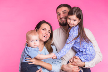 Cute family posing and smiling at camera together on pink background