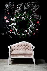 A huge chalk board with a painted wreath and a sign for a St. Valentine's day and a rich beige sofa under it. Valentine's Day theme. Place for text, logo.