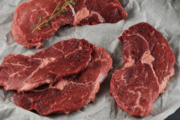 Some raw beef steaks on parchment paper. On one of the steaks is a twig of thyme. View from above. Close-up. Macro photography. 