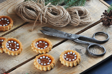 Christmas composition of fir branches, cones, cookies, wooden Christmas toys. In the frame scissors and a skein of braid. Wooden background. Close-up. Macro photography.