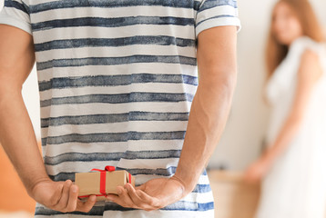 Man holding present for girlfriend behind his back at home