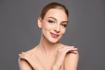 Portrait of beautiful young woman with clear skin on grey background