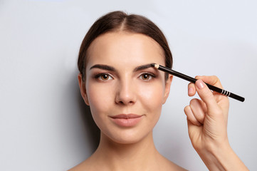 Fototapeta premium Young woman undergoing eyebrow correction procedure on light background