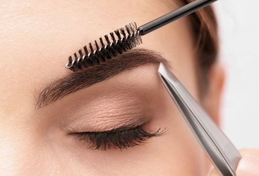 Young woman correcting shape of eyebrows, closeup