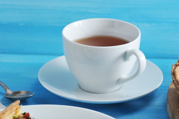 White porcelain cup and saucer. In the cup black tea. In the frame, a teaspoon. Blue wood background. View from above. Close-up. Macro photography.