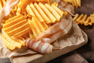 Crispy potato chips with bacon on wooden board, closeup