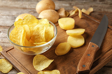 Bowl with crispy chips and raw potato on wooden table