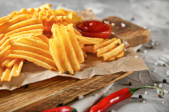 Crispy potato chips with chili pepper and sauce on wooden board, closeup