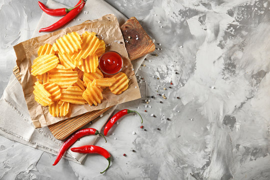 Crispy potato chips with chili pepper and sauce on wooden board