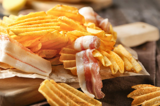 Crispy potato chips with bacon on wooden board, closeup