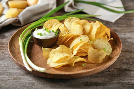 Crispy potato chips with green onion and sour cream on wooden plate
