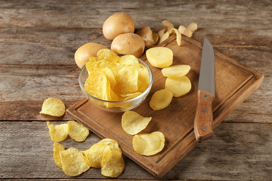 Bowl with crispy chips and raw potato on wooden table