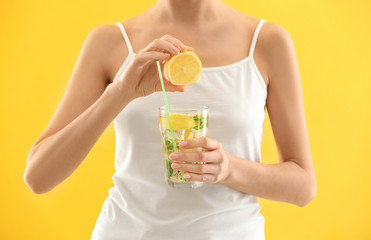Young woman squeezing juice into glass with lemonade on color background