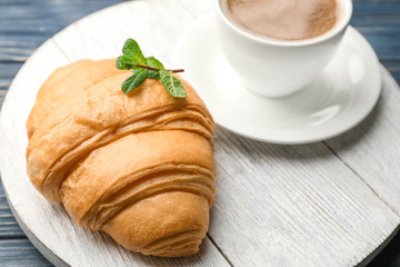 Delicious croissant with cup of coffee on wooden board