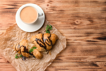 Delicious croissant with chocolate and cup of coffee on table