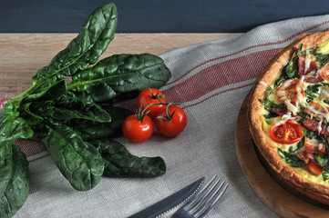 In the frame, a piece of pie quiche with spinach and bacon, cherry tomatoes, spinach greens and...