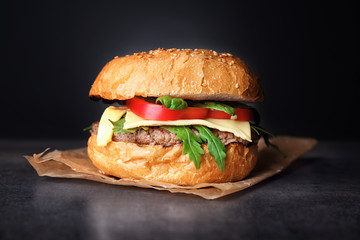 Tasty burger on table against dark background