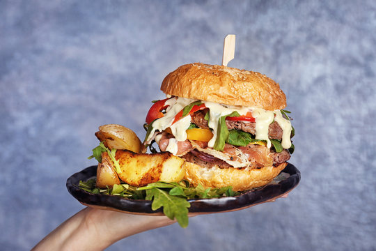 Woman holding plate with tasty burger and potatoes, closeup